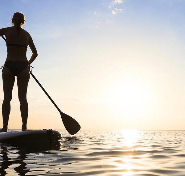 Girl stand up paddle boarding (sup) on quiet sea at sunset Kenya