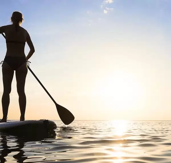 Girl stand up paddle boarding (sup) on quiet sea at sunset Kenya